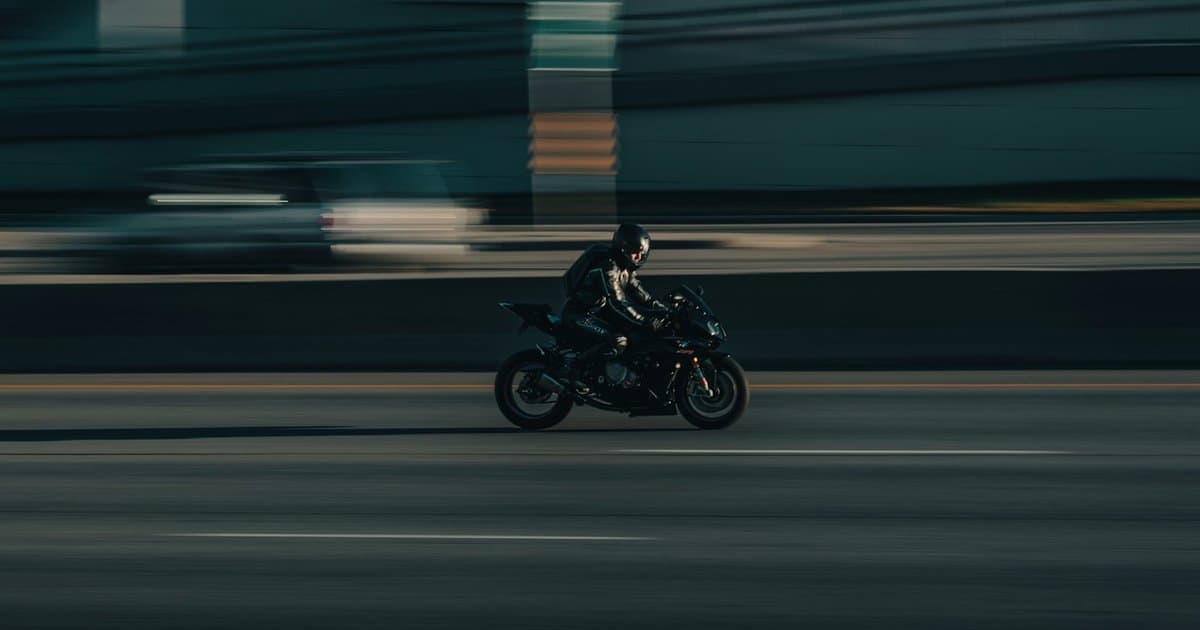 Motociclista com capacete e jaqueta de proteção pilotando em alta velocidade em uma via urbana, representando os riscos cobertos pelo seguro de moto